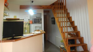 Una escalera de madera que conduce a una zona superior con cocina y televisor en primer plano.