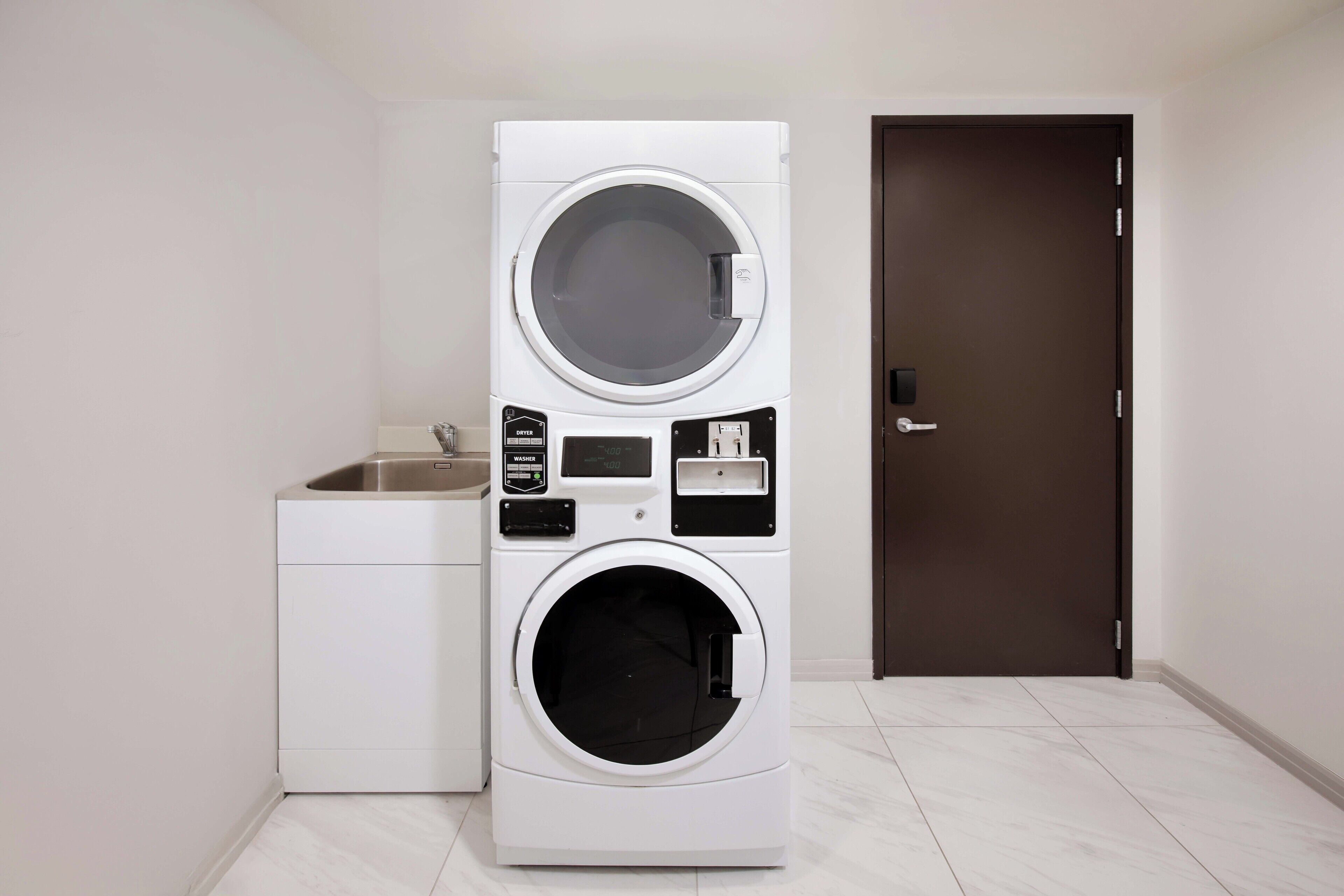 A compact laundry area with a stacked washer and dryer, a small sink, and a dark door.