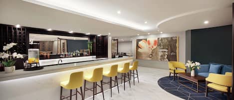 Un moderno vestíbulo de hotel con una zona de bar, taburetes amarillos, un sofá azul y una mesa de centro.