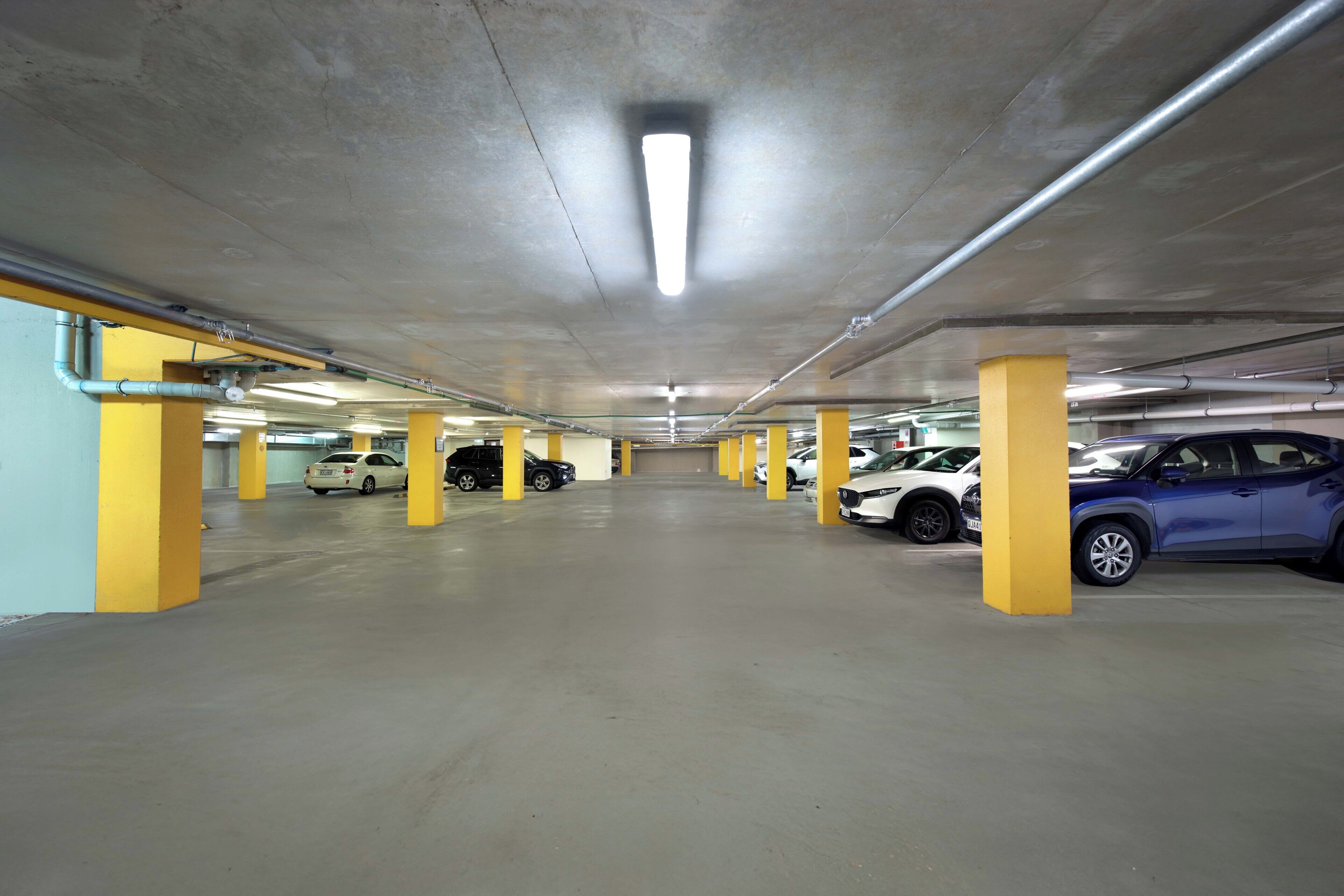 A multi-level parking garage with yellow pillars, concrete floors, and overhead lighting.