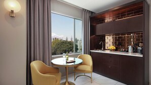 A modern kitchen with a round table and two chairs, a large window with curtains, and a view of buildings and trees. - Swiss-Belhotel Napier (Napier)