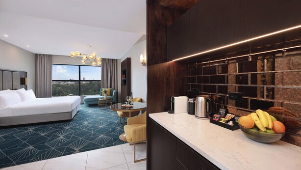 A modern hotel room with a large bed, a dining area, and a kitchen counter with fruit. - Swiss-Belhotel Napier (Napier)