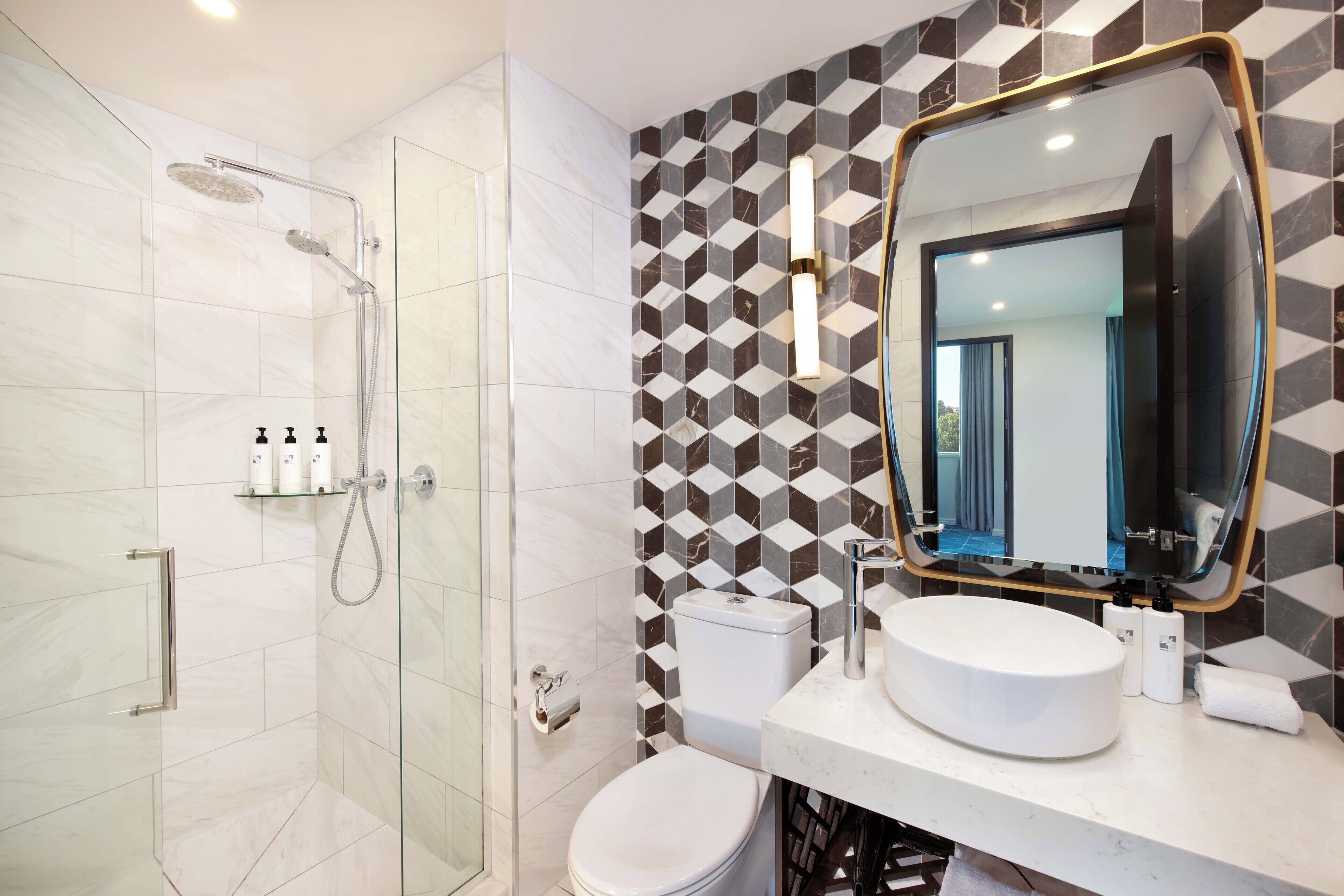 A modern bathroom with a glass-enclosed shower, a toilet, and a sink with a large mirror.