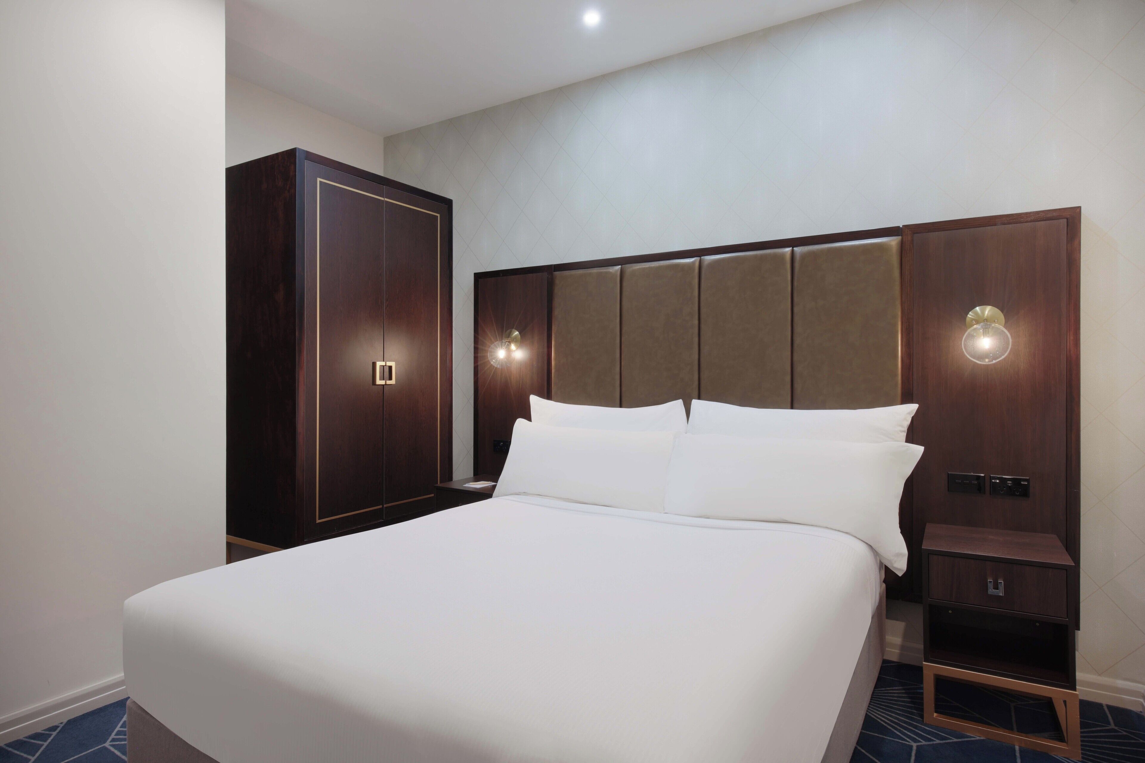 A hotel room with a large bed, a wardrobe, and a nightstand with a lamp.