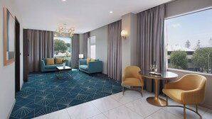 A modern hotel room with a geometric patterned carpet, two sofas, a round table with chairs, and large windows offering a city view. - Swiss-Belhotel Napier (Napier)