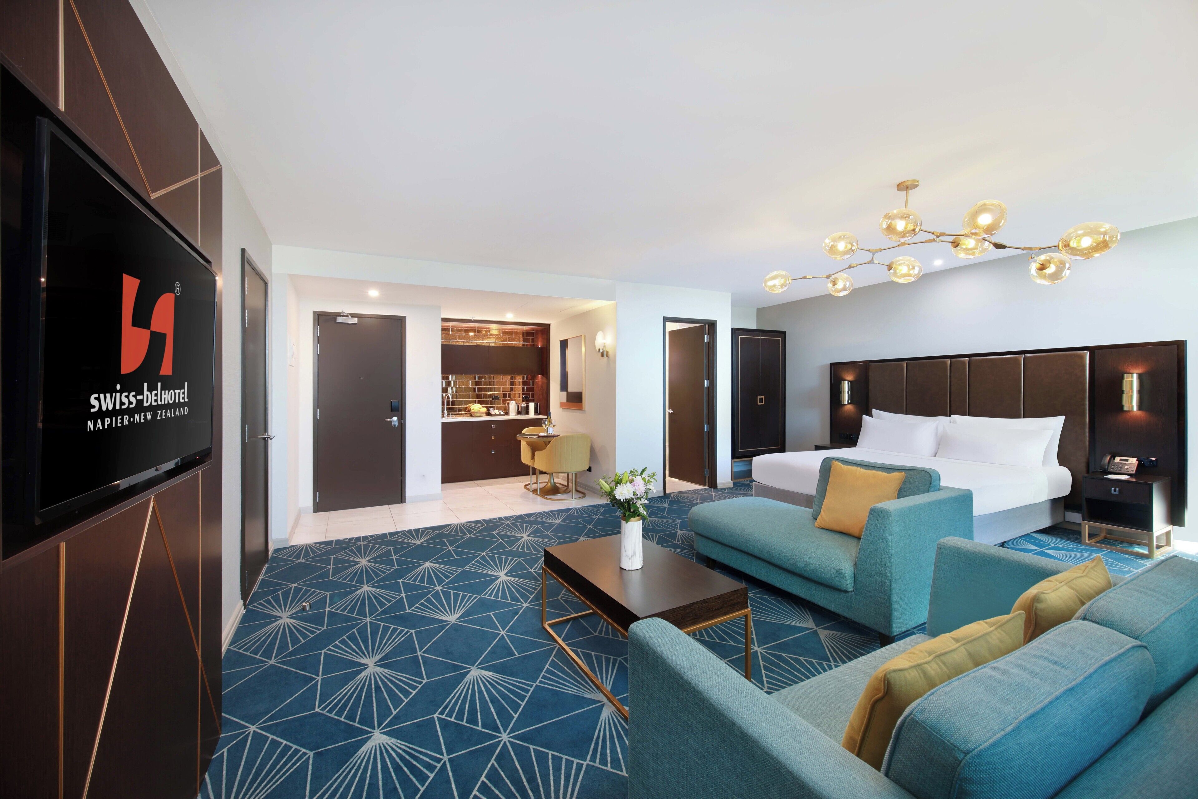 A hotel room with a modern design, featuring a large bed, a sofa, a coffee table, and a TV mounted on the wall.