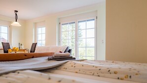 A bedroom with a bed, a bedside table with a lamp, and large windows. - Apartment at Landhof Rothenberg - terrace with views of meadows and forests (Rothenberg)