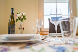 Une table à manger dressée avec des assiettes, des couverts et des verres à vin, une bouteille de vin et un vase rempli de fleurs.