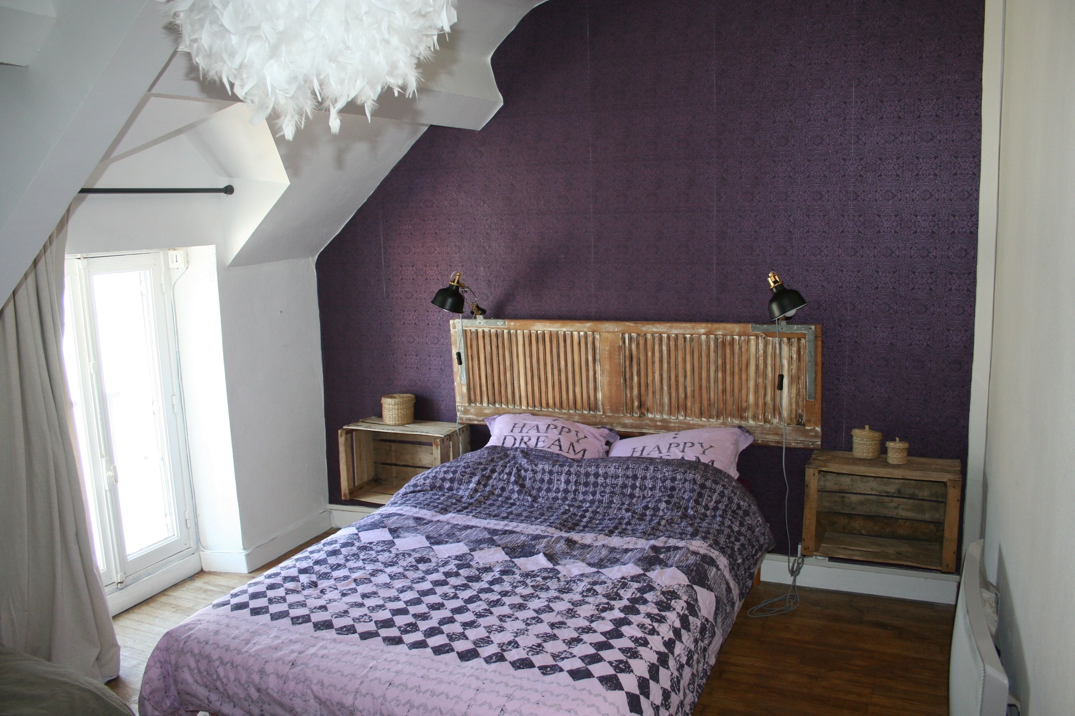 A bedroom with a sloped ceiling, a bed with a patterned bedspread, two bedside lamps, and a headboard with a wooden texture.