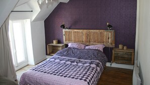 Ett sovrum med ett sluttande tak, en säng med ett mönstrat överkast, två sänglampor och en sänggavel med trästruktur.