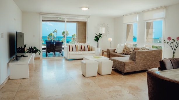 Ein geräumiges Wohnzimmer mit großem Fenster zum Meer, ein weißes Sofa, ein braunes Sofa und ein Essbereich.
