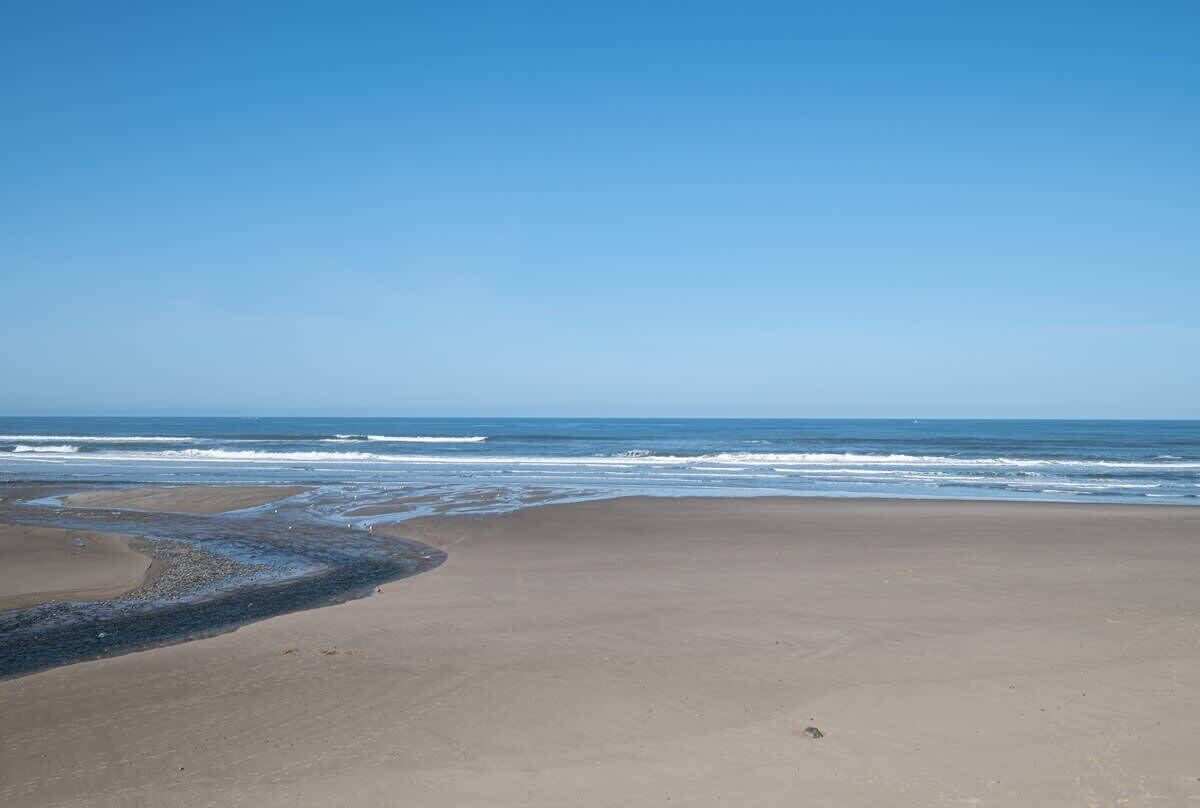 Ein weiter Sandstrand mit sanften Wellen und blauem Himmel.