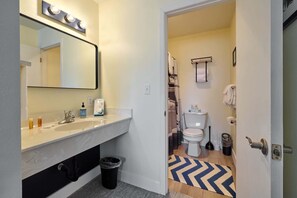 Een badkamer met een wit wastafelmeubel, spiegel en wc, en een zwarte prullenbak.