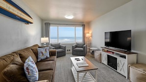 Habitación de hotel moderna con un amplio ventanal que ofrece vistas al océano, un sofá cómodo, un televisor de pantalla plana y una pequeña mesa.