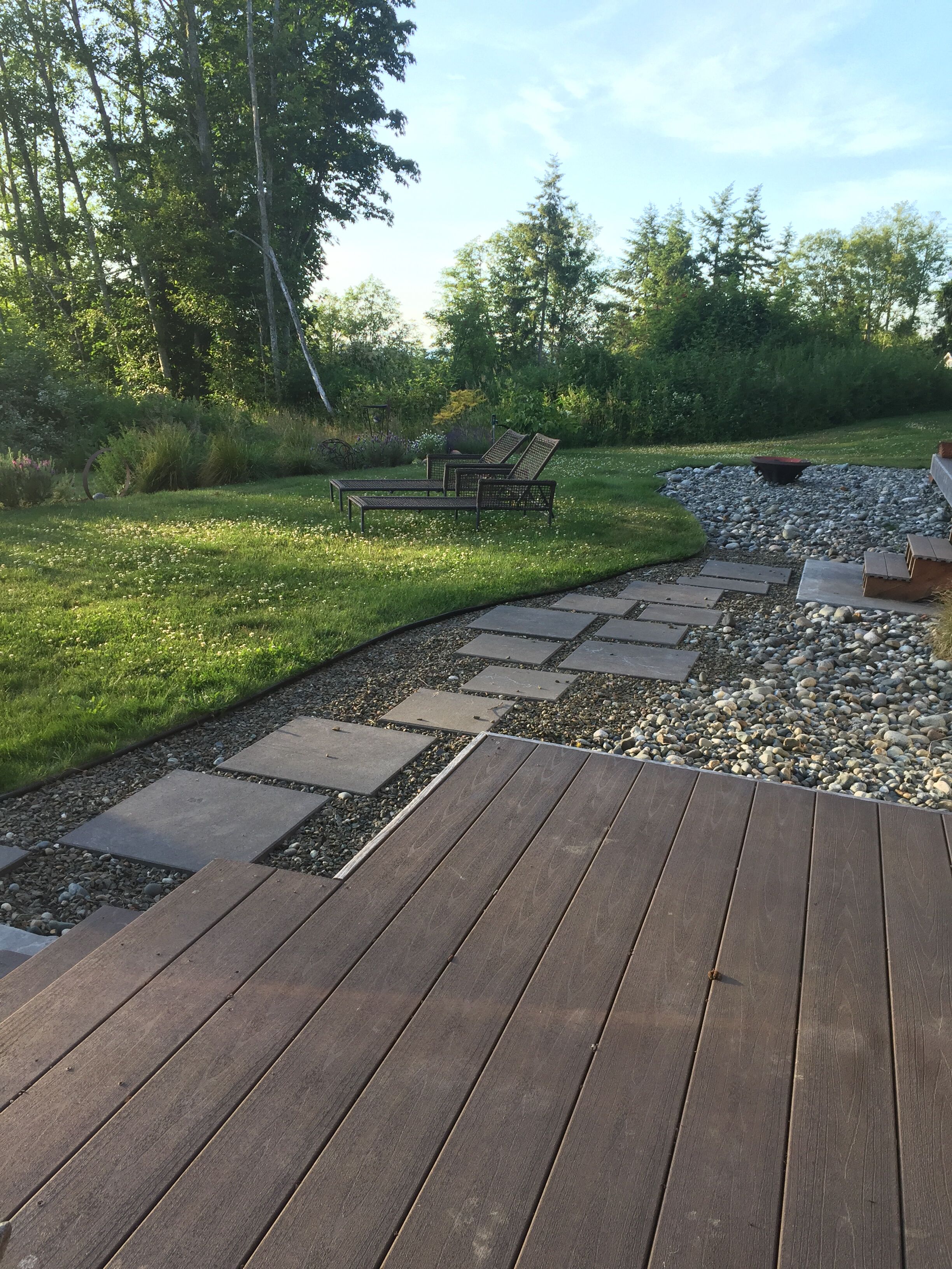 A wooden deck with a stone pathway leading to a seating area with two lounge chairs.
