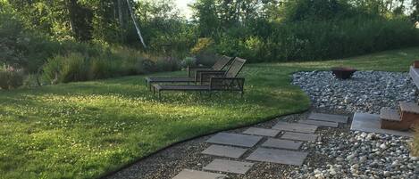 A wooden deck with a stone pathway leading to a seating area with two lounge chairs.