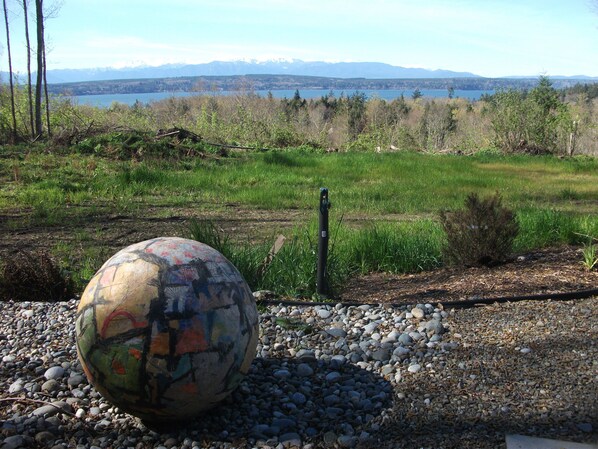 A large, colorful spherical sculpture in a gravel area with a view of a lake and mountains in the background. - Spectacular View! Romantic! Special 50% off per month, 25% off per week! (Hansville)