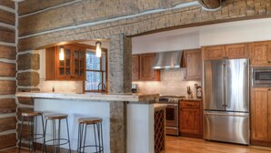 Eine Küche mit einer Steinwand, Holzschränken, einem Edelstahlkühlschrank und einer Bar mit Hockern.