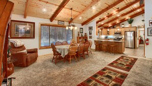 A spacious living room with a dining area, wooden ceiling beams, and a kitchen in the background. - (36) Larkspur Lair at The Redwoods In Yosemite (Yosemite National Park)