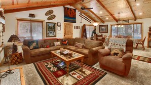 A cozy living room with a wooden ceiling, a fireplace, a sofa, a coffee table, and a dining area with chairs. - (36) Larkspur Lair at The Redwoods In Yosemite (Yosemite National Park)