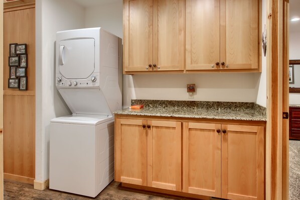 A laundry room with a front-loading washer and dryer, wooden cabinets, and a granite countertop. - (36) Larkspur Lair at The Redwoods In Yosemite (Yosemite National Park)