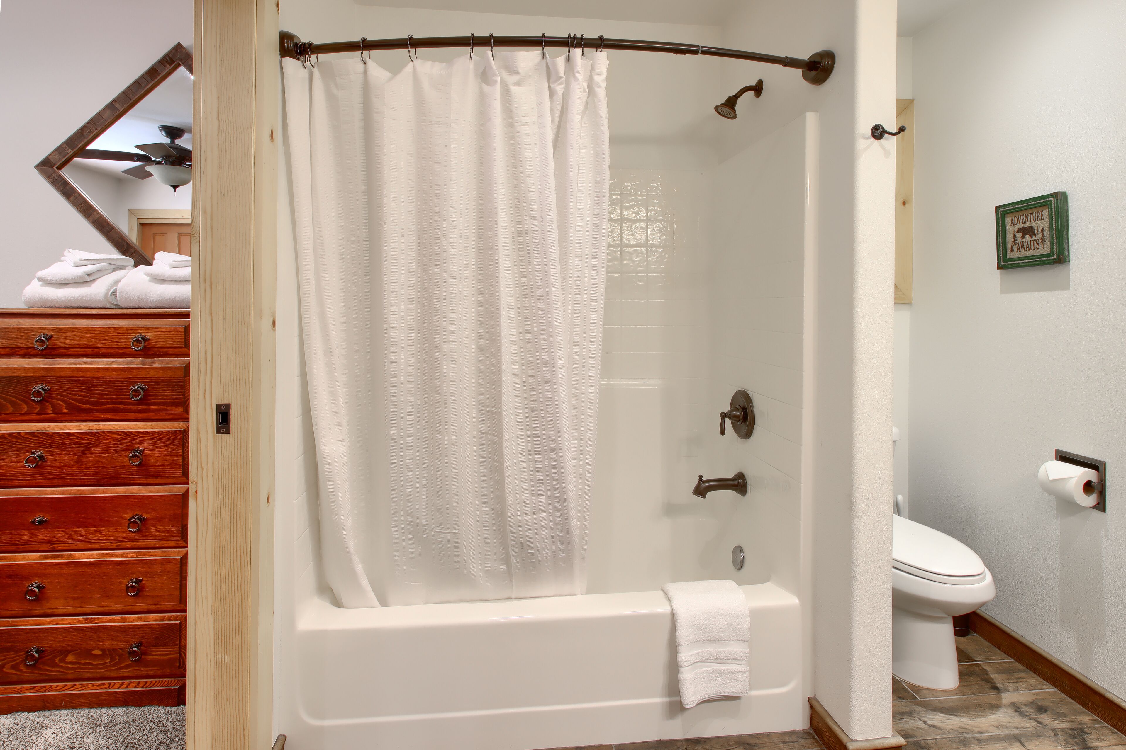 A bathroom with a glass-enclosed shower, a wooden dresser, and a toilet.