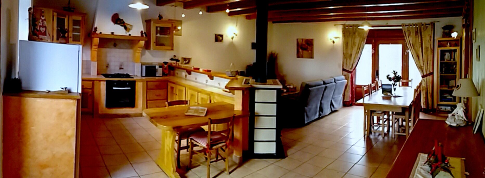 Een keuken met houten kastjes, een eethoek met tafel en stoelen, en een bank in de woonkamer.