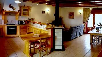 Een keuken met houten kastjes, een eethoek met tafel en stoelen, en een bank in de woonkamer.