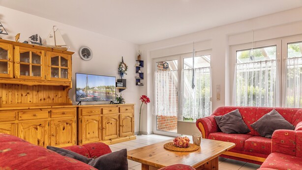Ein Wohnzimmer mit einem Holzkabinett, einem roten Sofa, einem Holztisch und einem Fernseher.
