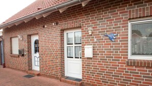 Ein Backsteinhaus mit weißer Tür, einem Fenster mit Vorhang und einem Briefkasten.