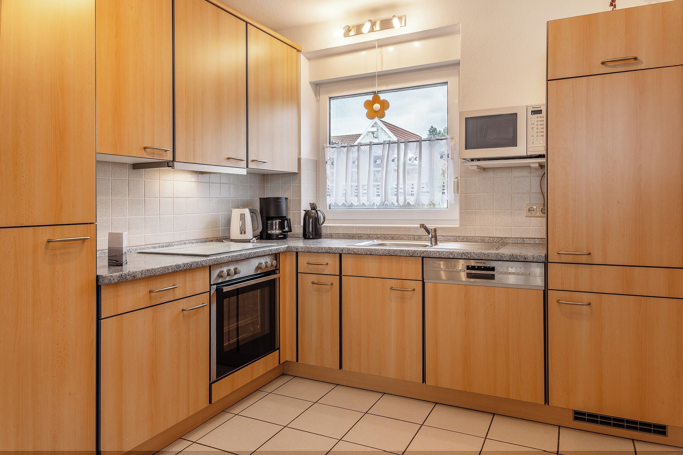 Eine moderne Küche mit Holzausstattung, einem Backofen, einer Mikrowelle und einem Fenster mit Blumenornament.