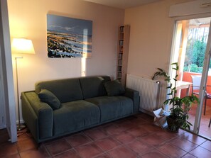 Relax in this inviting living room with a sofa, floor lamp, and bookshelf, plus a sliding door to an outdoor space with a table and chairs.