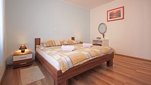A bedroom with a wooden bed, a nightstand, a bedside table, a mirror, and a framed picture on the wall.