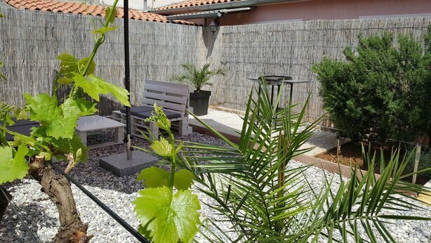 A patio area with a wooden bench, a table, and a potted plant.