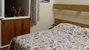 A bedroom with a wooden headboard, a floral bedspread, a window with curtains, a small bedside table, and a framed picture on the wall. -  * RUNNING AND WALKING BEACH * enclosed garden * CLIM * WIFFI * PARKING * (Saint-Cyprien)