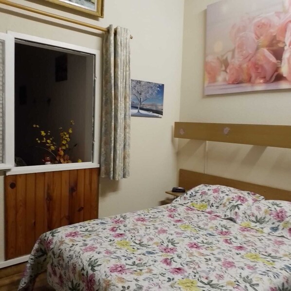 A bedroom with a wooden headboard, a floral bedspread, a window with curtains, a small bedside table, and a framed picture on the wall. -  * RUNNING AND WALKING BEACH * enclosed garden * CLIM * WIFFI * PARKING * (Saint-Cyprien)