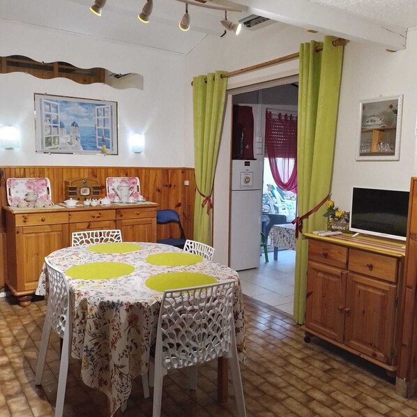 A cozy room with a wooden dining table, chairs, a television, and a cabinet. -  * RUNNING AND WALKING BEACH * enclosed garden * CLIM * WIFFI * PARKING * (Saint-Cyprien)