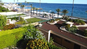 Un hotel a la costa amb vista al mar, un passeig marítim amb palmeres i jardins paisatges.