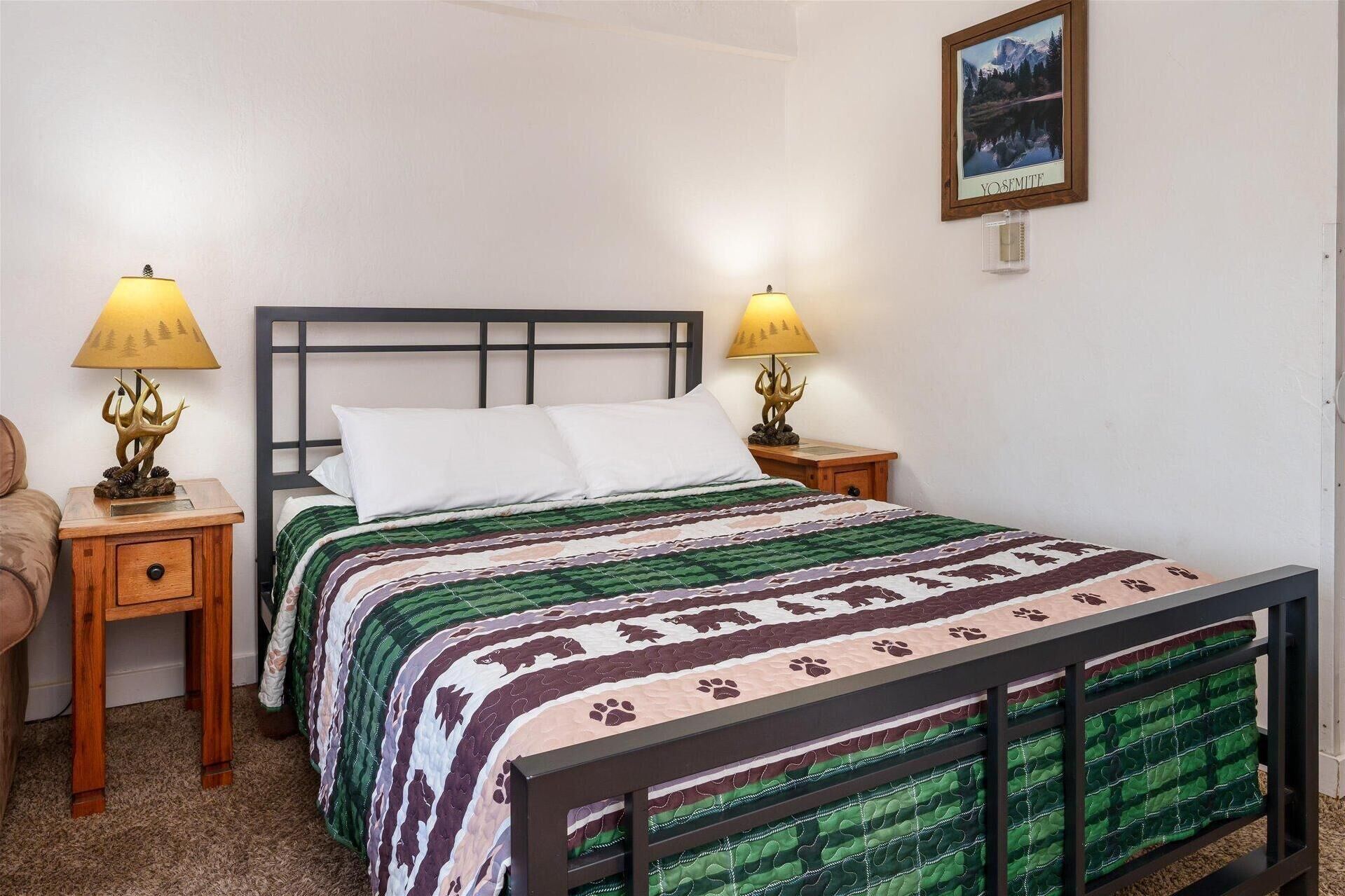A neatly made bed with a patterned bedspread, two bedside lamps with animal designs, a framed picture on the wall, and a wooden nightstand with a drawer.