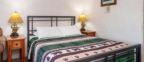 A neatly made bed with a patterned bedspread, two bedside lamps with animal designs, a framed picture on the wall, and a wooden nightstand with a drawer.