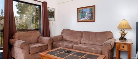 Un salón con un sofá de cuero marrón, una mesa de centro de madera, un cuadro enmarcado en la pared y una lámpara sobre una mesita de noche de madera.