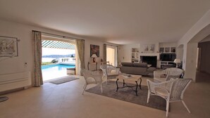 A spacious living room with a pool view, a sofa, and wicker chairs. - Villa with private pool - 10 people - Sea view - Air conditioning - WiFi - Sainte Maxime - Rated 4* (STE MAXIME)