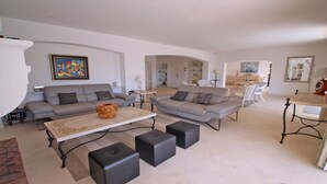 A spacious living room with two sofas, a coffee table, and black ottomans. There is a painting on the wall and a dining area in the background. - Villa with private pool - 10 people - Sea view - Air conditioning - WiFi - Sainte Maxime - Rated 4* (STE MAXIME)