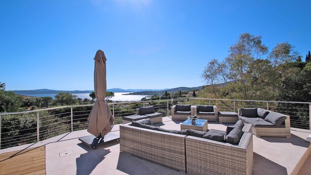 A terrace with wicker furniture, a table, and an umbrella, overlooking a scenic landscape with water and hills. - Villa with private pool - 10 people - Sea view - Air conditioning - WiFi - Sainte Maxime - Rated 4* (STE MAXIME)