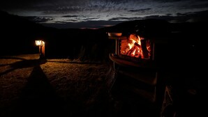 Ein Campingplatz bei Nacht mit einem brennenden Feuer in einer Metallfire-Pit, umgeben von einer dunklen Landschaft.