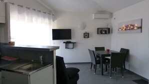 A modern kitchen with a dining area, a flat-screen TV, and a small shelf with decorative items.