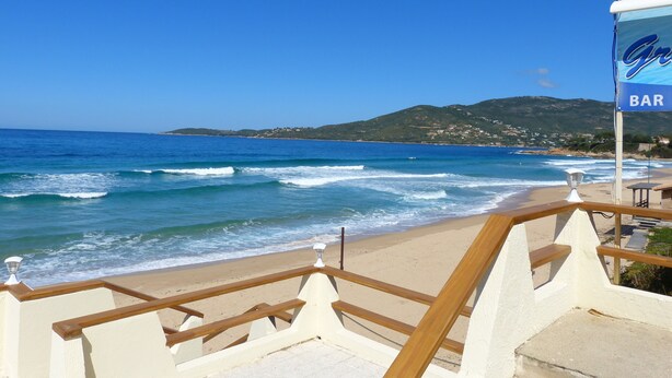 A beach view with a wooden railing, a sign for a bar, and a mountain in the background.
