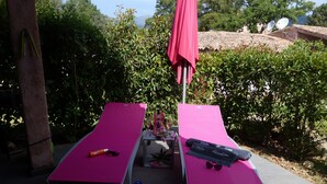 Two sun loungers with pink cushions, a red umbrella, and a pair of blue flip-flops on the ground.