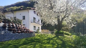 A white building with a balcony, surrounded by a well-maintained lawn and a tree with white blossoms. - The Best Place To Visit Como Lake (Barni (COMO))