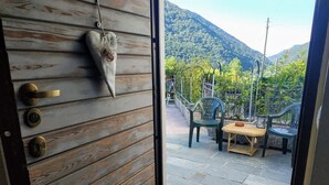 A wooden door with a heart-shaped decoration, a doormat with "WELCOME" text, and a view of an outdoor seating area with chairs and a table, overlooking a mountainous landscape. - The Best Place To Visit Como Lake (Barni (COMO))